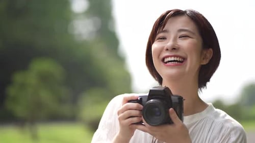Happy Woman with Camera Smiles in Green Setting