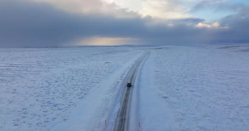 Auto überquert verschneite Straße mit bewölktem Horizont