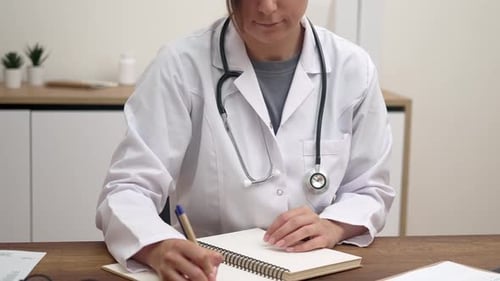 Female Doctor Writing in Notebook at Desk