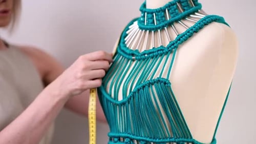 Costureira mede corpete de vestido verde de macramê em manequim trabalhando em um ateliê de moda