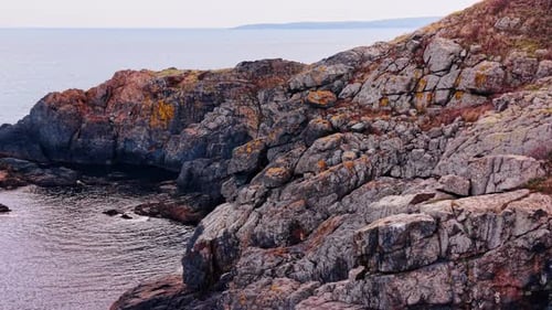 Grey rocks descend into the waterscape. Footage above the rocky shore covered with dry grass.