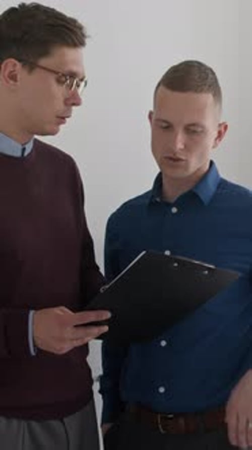 Vertical of Two Male Colleagues Discussing Document while Working at Office