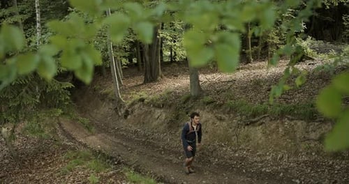 Weitwinkelaufnahme eines Wanderers, der auf einem von grünen Bäumen umgebenen Waldweg den Hügel hinaufgeht