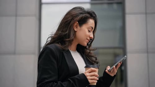 Woman Uses Phone with Coffee in Urban Setting