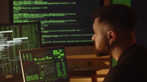 A Data Scientist Analyzes Data From Monitors That Display Program Code A Male Programmer Sits in the