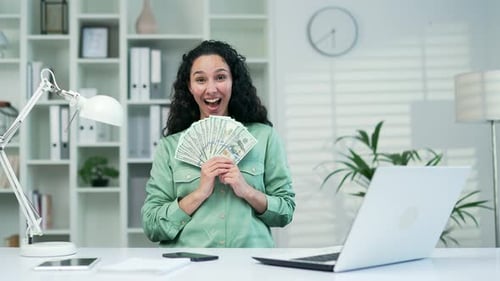 Fröhliche Freude, junge Frau, freut sich, zu verdienen oder zu gewinnen, zeigt viele Dollarscheine, Bargeld, schaut in die Kamera.