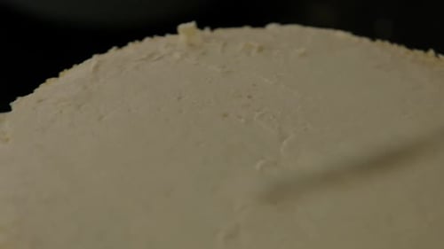 Close-up of frosting the top of a vanilla cake with a spatula.