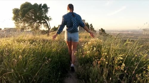 Woman Walking Toward Ruins in Rural Landscape at Sunset