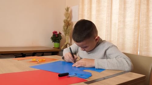 Focused Boy Drawing on Blue Construction Paper