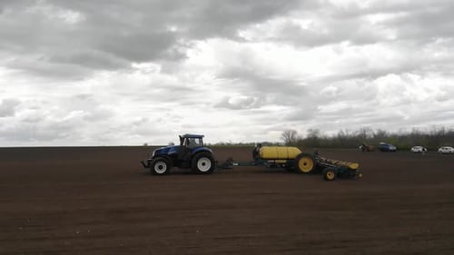 Blue tractor planting sunflower with yellow planter on the field in Ukraine