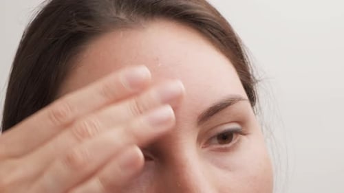 Woman Applies Skincare to Forehead Close Up