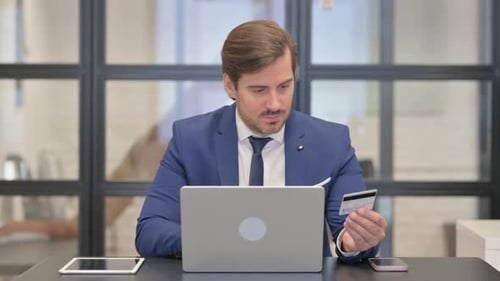 Man Using Credit Card and Laptop in Office