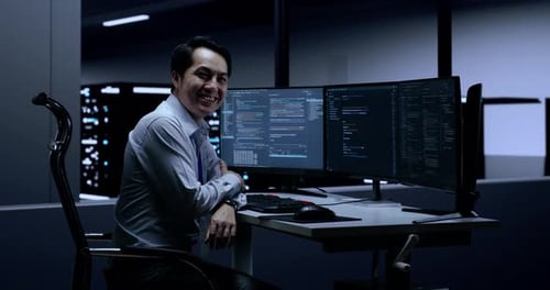 Asian Male Programmer Smiling To Camera While Writing Code By Desktops In The Server Room