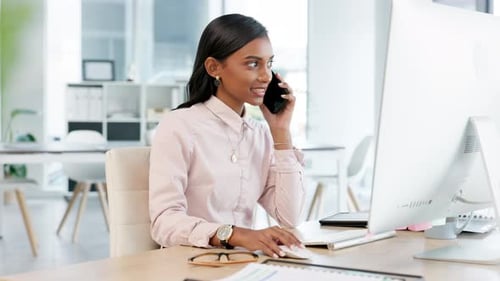 Young business woman talking on a phone while working on her computer in the office