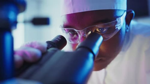 Scientist Using Microscope in Dark Blue Lab