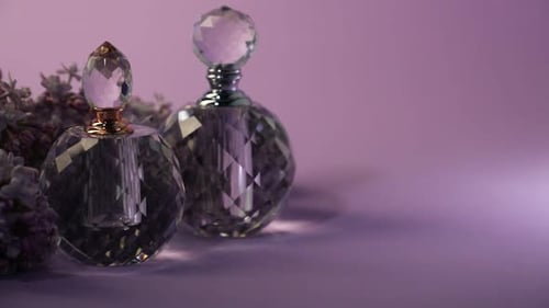 Perfume bottles and beautiful lilac flowers on violet background, space for text. Changing direction