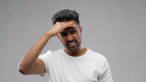 Frustrated man with hand on forehead against grey