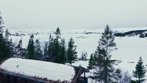 Mountain Cabin With Pine Trees Overlooking The Frozen Lake At Winter. - aerial shot