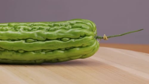 Une gourde amère, un légume souvent utilisé comme ingrédient en cuisine, est posée sur une table en bois.