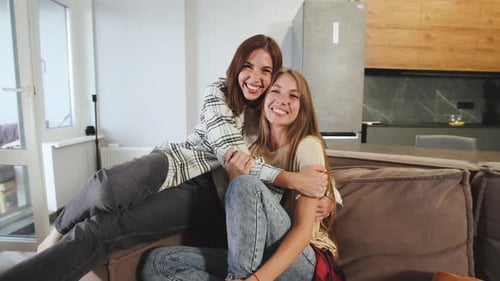 Two Friends Smiling Together on Couch Indoors