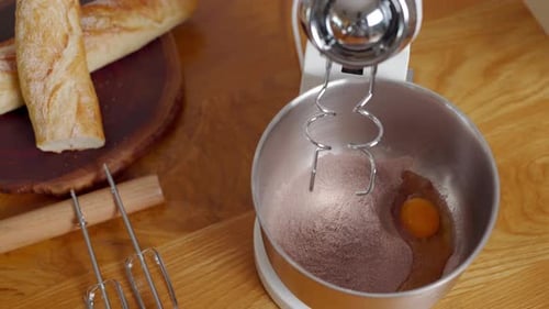 Hands putting ingredients for delicious cake in bowl, stand mixer whisking batter