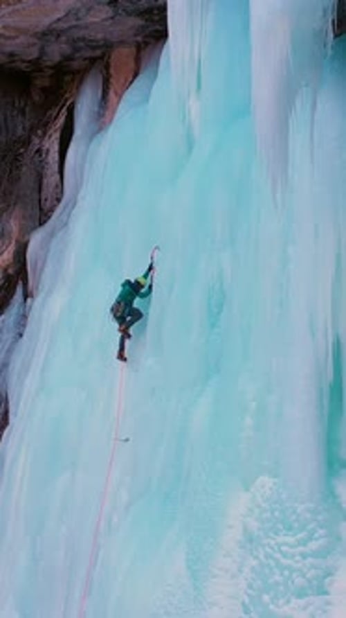 Bergsteiger führt beim Eisklettern auf gefrorenen Wasserfällen Vertikales Video aus der Luft