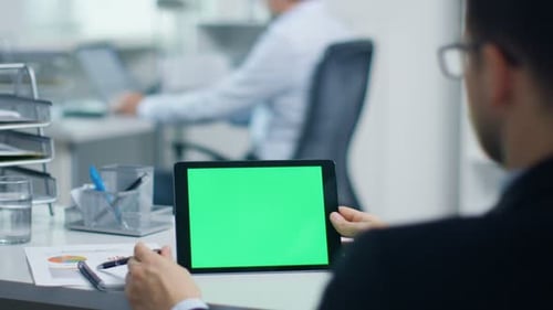 Businessman Uses Tablet Computer with Green Screen, He Swipes and Touches Screen. In the Background