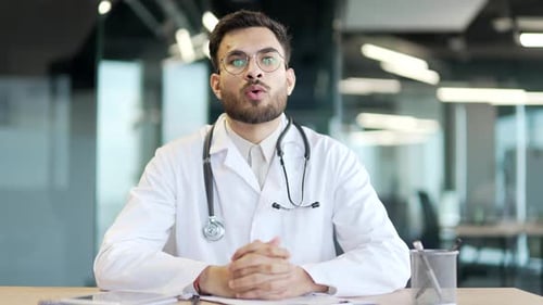 Webcam view. Male doctor watching video call conference looking at camera in hospital clinic office.