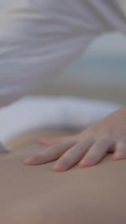 Hands of Masseuse Spreading Oil in Clients Back in Massage at the Beach Outdoors