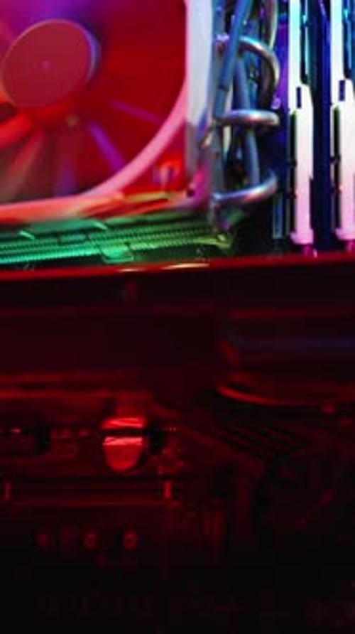 Vertical video. In the darkness, a gaming desktop PC shimmers with rainbow light, close-up.