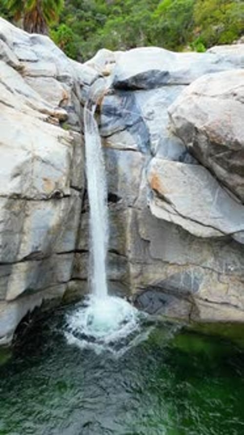 Aerial drone view of a small waterfall cascading between massive rocks into a natural pool in Baja C