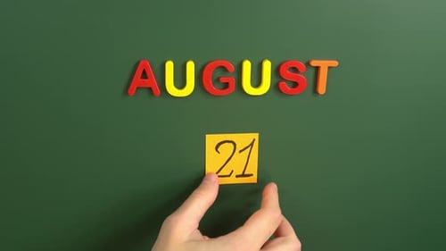 Hand sticking a sticker 21 August calendar day on school board. 21 date of august. Twenty first day