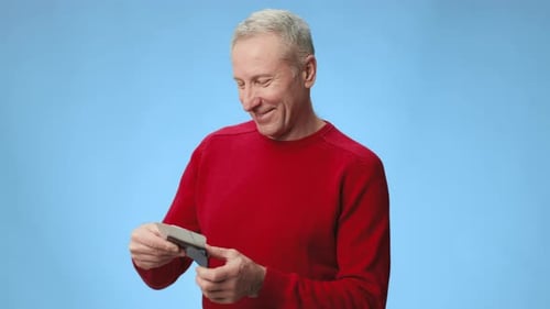 Homme regardant une carte tout en portant un pull rouge sur fond bleu en images