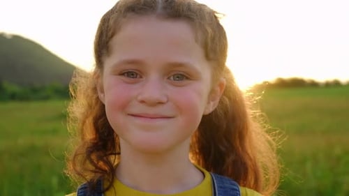 Portrait of smiling adorable little girl kid standing in green field and enjoying summer nature
