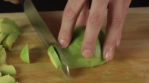 Hands of middle man european slices a avocado with kitchen knife on cutting board, front side view