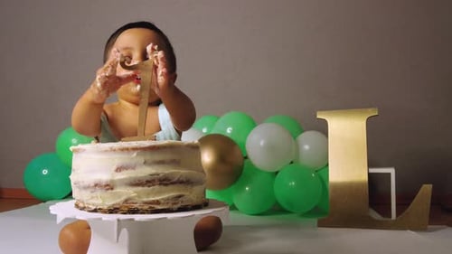 Cute latin baby toddler celebrating his 1st year removing the number one off his cake with green bal