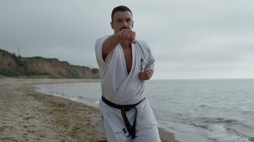 Karate-Mann trainiert Kampffähigkeiten am Sandstrand aus nächster Nähe. Starker Sportler