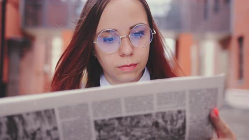 Thoughtful Young Woman Reading Newspaper on Street
