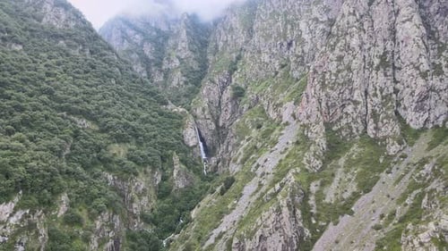 drone shot of waterfall in the middle of caucasian mountains with rocks clouds and green trees