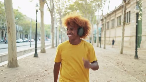 Young African American man dancing in the street while listening to music on his headphones