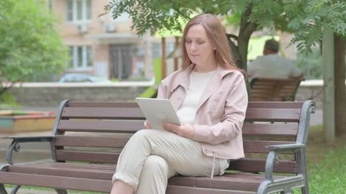 Woman Using Tablet on Park Bench in City