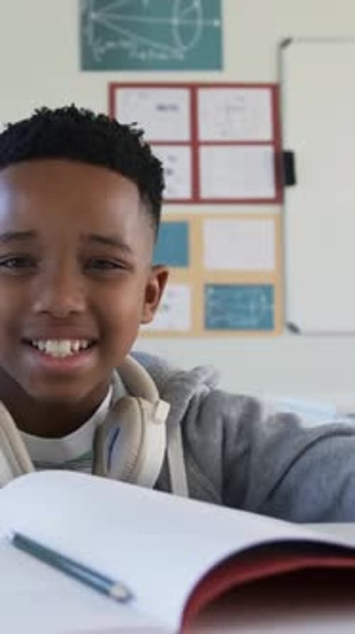 Vertical video: Glancing, hooded student grabbing pencil, checking notes in classroom, copy space