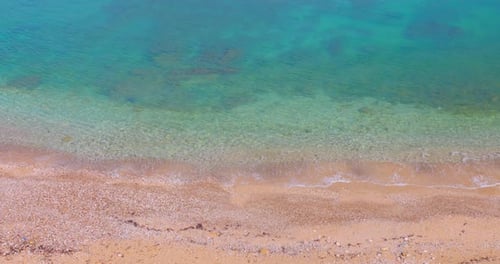 Aerial shot of crystal-clear turquoise waters lapping onto a serene sandy beach