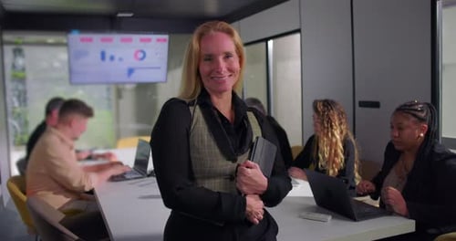 Smiling businesswoman standing confidently with tablet in hand during office meeting,