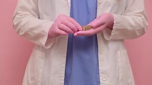 Woman doctor holding euro cent coins, studio pink background. Nurse in uniform with stethoscope
