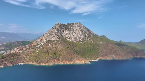 Turquoise Waters Lapping Against a Rugged Mountain Create a Serene Scene Sunlight Bathes the Slopes