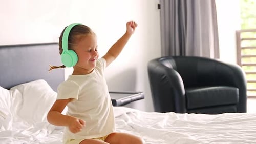 Smiling Girl with Headphones Dancing on a Bed