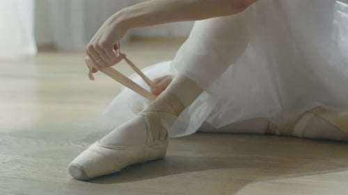 Ballerina tying ribbons of her ballet slippers