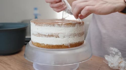The pastry chef removes the cling film from the prepared cake for decoration.