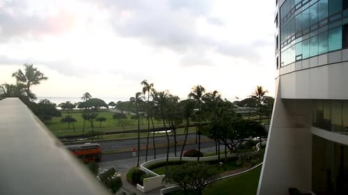 Balcony view of cars and red bus crossing the street. Green palm trees in the background and white c